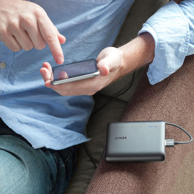A phone held and operated by someone sitting in a couch. The PowerCore 13000 is connected to this phone and is charging it